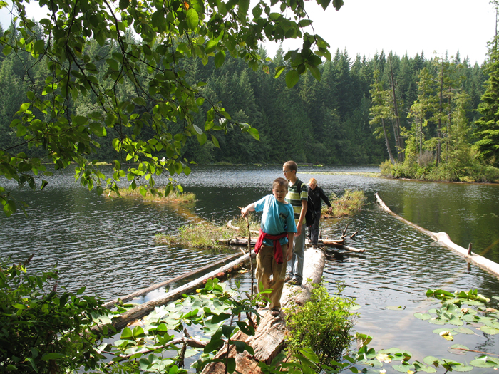 The kids walk out on a tree trunk that goes out into a lake along the trail
